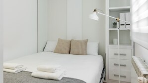 Un lit bien fait, avec du linge de lit blanc, une lampe de chevet et un meuble de rangement doté de tiroirs.