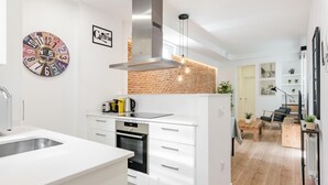 Une cuisine moderne avec des meubles blancs, une hotte de cuisinière en acier inoxydable et un mur d’accent en briques.