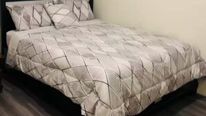 Een enkel bed met een bedspreider met een geometrisch patroon en passende kussens, een donker hoofdbord en een houten vloer.