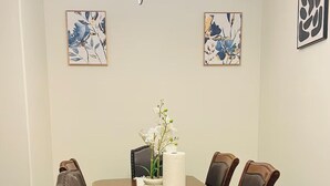 Een eetkamer met een houten tafel, zwarte stoelen, een kroonluchter en bloemkunst aan de muren.