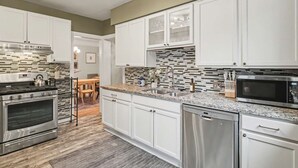A modern kitchen with white cabinetry, a granite countertop, stainless steel appliances, and a patterned backsplash. - Hot Tub - Game Room - Professional Design-Backyard (University Heights)