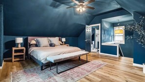 A bedroom with a bed, bedside tables, a ceiling fan, a window, and a plant. - Hot Tub - Game Room - Professional Design-Backyard (University Heights)