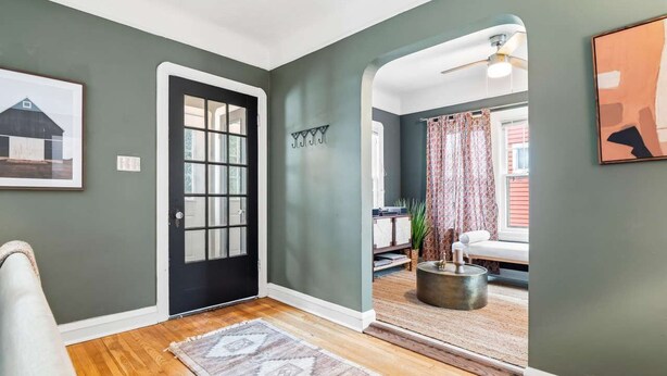 A hallway with a black door, a patterned rug, and a view into a living room with a couch and curtains. - Hot Tub - Game Room - Professional Design-Backyard (University Heights)