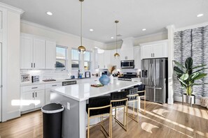 A modern kitchen with white cabinetry, stainless steel appliances, a central island with bar stools, and pendant lighting.