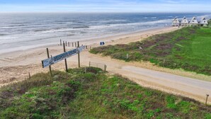 Vista de la playa con un letrero que indica Surfside Beach, un sendero de tierra y cabañas de playa al fondo.