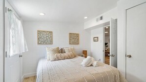 Un dormitorio con cama, dos paneles decorativos en la pared, una puerta y una ventana con cortina.