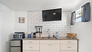 Uma cozinha compacta com armários brancos, micro-ondas, cafeteira e uma TV de tela plana fixada acima da pia.