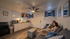 Uma sala de estar moderna com sofá, mesa de centro, televisão e área de cozinha com armários e eletrodomésticos.