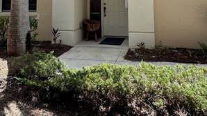 Une maison à la façade beige, avec un palmier et un petit porche abritant une niche pour chien.