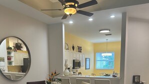Un coin repas avec une table en verre, des chaises et un ventilateur de plafond.