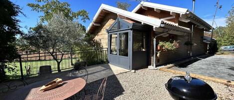 Eine moderne Außenpatio mit rundem Tisch und Stühlen, einem Grill und einem kleinen, abgeschlossenen Bereich mit einer Tür.