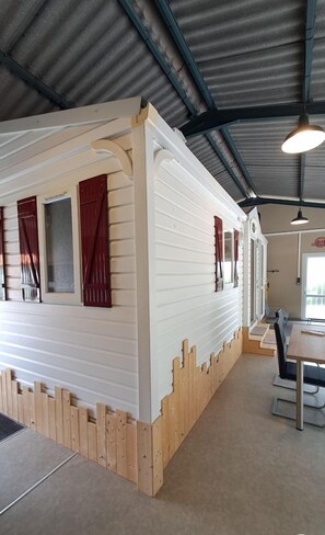 A spacious room with a high ceiling, wooden flooring, and a dining area with tables and chairs.