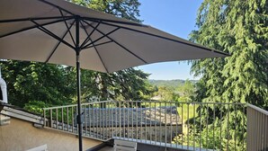 A patio with a table and chairs, a large umbrella, and a view of a stone roof and trees. - Gîte 35 - SAINT-PIERRE-DE-TRIVISY (SAINT-PIERRE-DE-TRIVISY)