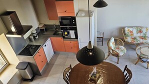 Kompakti keittiö moderneilla laitteilla, ruokapöytä tuoleineen sekä sohva valoisassa olohuoneessa.