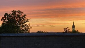 A sunset view from a rooftop with a brick wall in the foreground and a church spire in the background. - Gîte 35 - SAINT-PIERRE-DE-TRIVISY (SAINT-PIERRE-DE-TRIVISY)