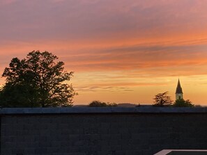Ein Sonnenuntergangsblick vom Dach mit einer Ziegelmauer im Vordergrund und einem Kirchturm im Hintergrund.