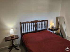 A hotel room with a wooden headboard, a bed with a red bedspread, a bedside table with a lamp, and a mirror. - Gîte 35 - SAINT-PIERRE-DE-TRIVISY (SAINT-PIERRE-DE-TRIVISY)