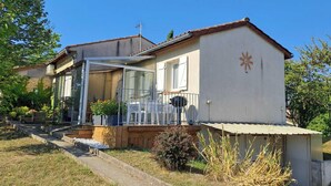 Une maison de plain-pied avec un balcon, un petit jardin et un ciel d’un bleu éclatant.