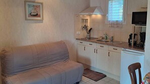 Une cuisine compacte équipée d’une cuisinière intégrée, d’un évier et d’une fenêtre avec un rideau. Un canapé se trouve dans le salon attenant.