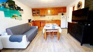 A compact living space with a sofa, dining table, and kitchenette. - Porto Frailis Apartment (Arbatax)