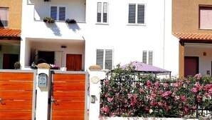 A white building with a gated entrance, a balcony with plants, and a flower wall. - Porto Frailis Apartment (Arbatax)