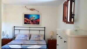 A bedroom with a bed, two bedside tables, a dresser, a painting, and a window with curtains. - Porto Frailis Apartment (Arbatax)