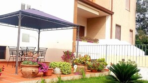 An outdoor patio area with a covered seating area, potted plants, and a staircase leading to a building. - Porto Frailis Apartment (Arbatax)