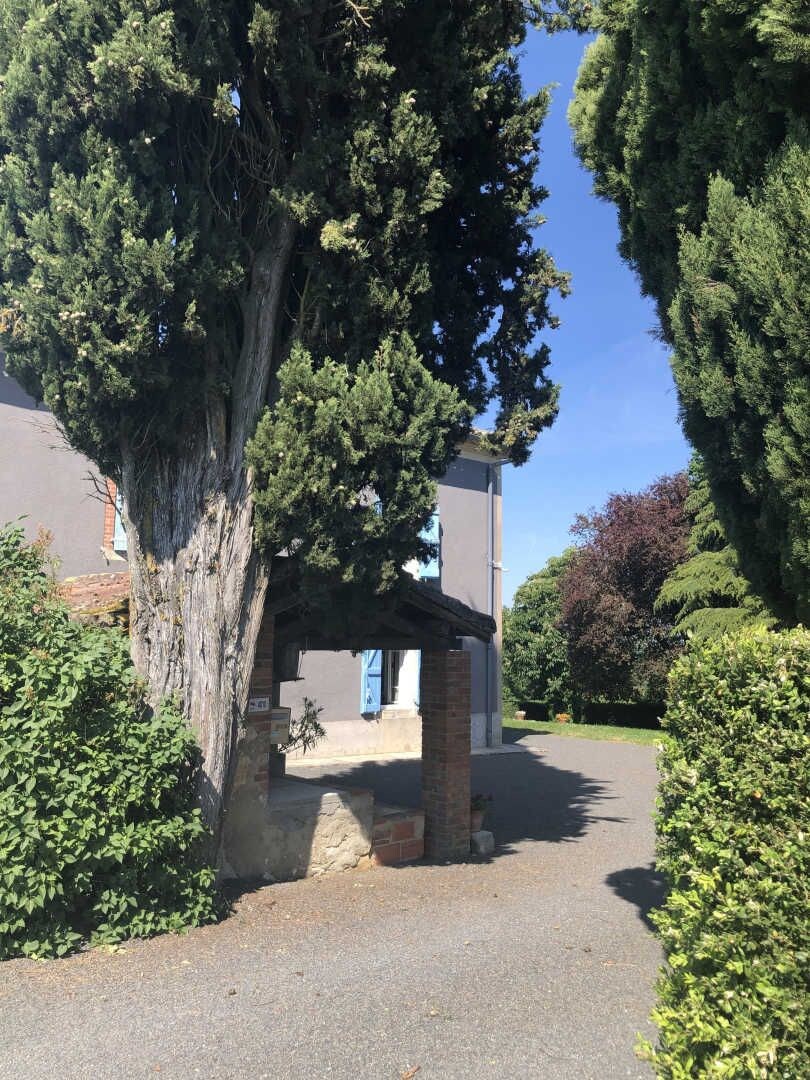 Un bâtiment avec une entrée en pierre, entouré d’arbres et d’arbustes.