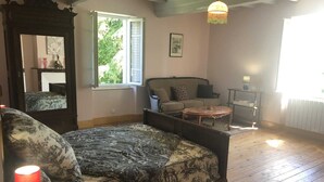 A cozy living room with a sofa, a chair, a round coffee table, a mirror, and a window with blinds. - Vors - GAILLAC - Gîte (GAILLAC)