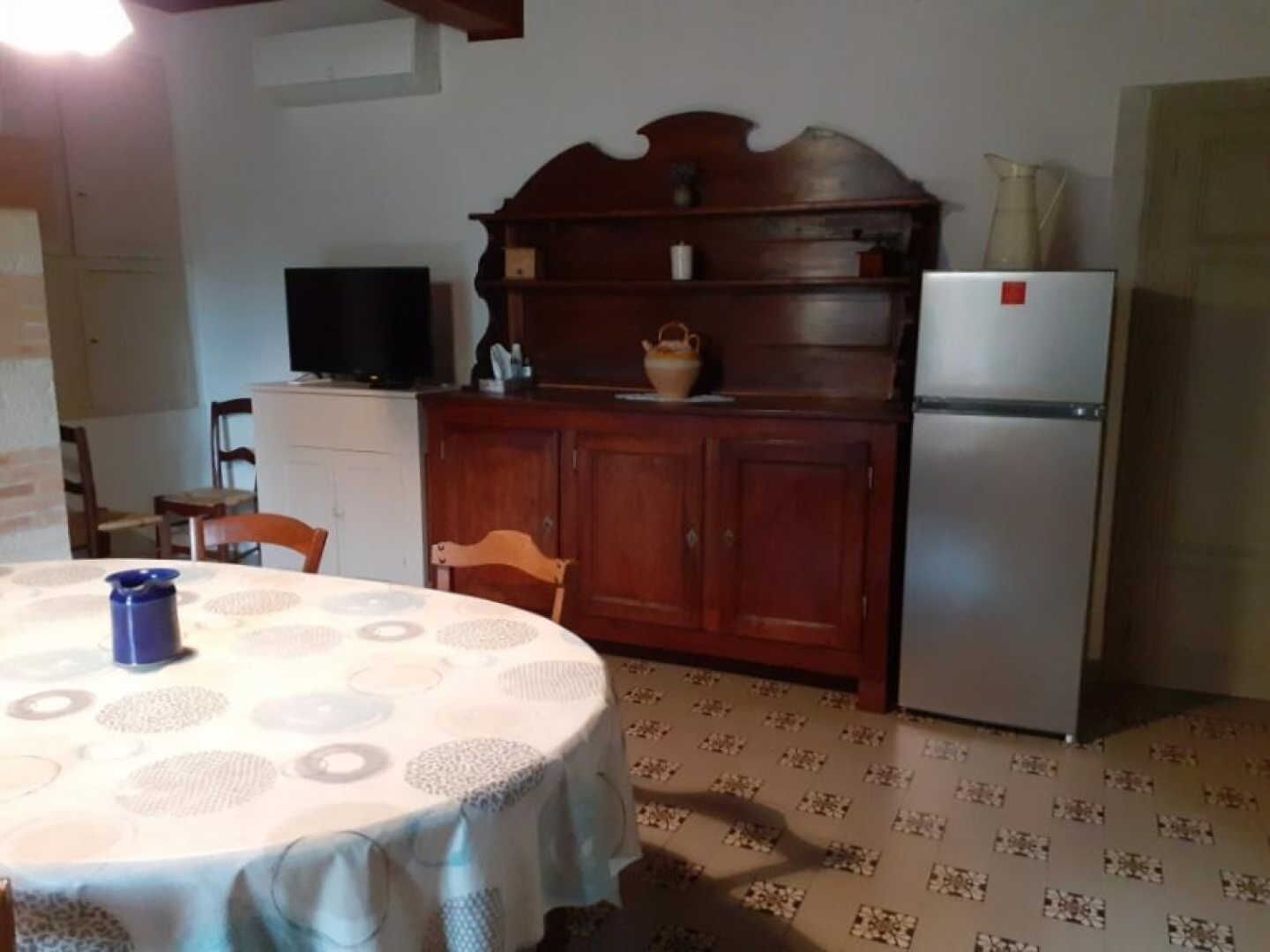 A dining area with a round table, chairs, a television, a cabinet, and a refrigerator.