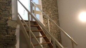 A staircase with wooden steps and white railings, leading to a room with a stone wall and a window.