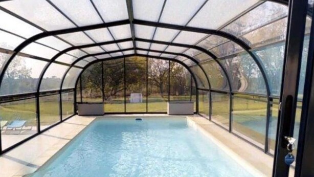 A covered swimming pool with a glass enclosure, a clear pool, and a view of the outdoors.