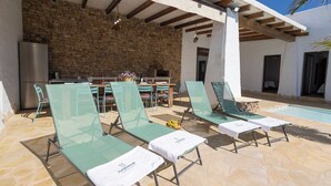 A poolside area with lounge chairs and a table, a stone wall, and a modern kitchen in the background.