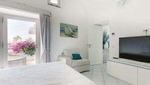 A modern hotel room with a large bed, a TV, a seating area with a chair, and a painting on the wall. - Villa Tirrena by My Villa Collection (Positano)