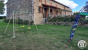 Un bâtiment rustique en pierre, doté d’un porche et d’une balançoire dans la cour.