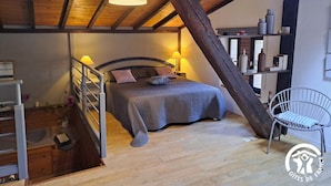 Une chambre confortable avec un plafond en bois, un lit doté d’une tête de lit, des lampes de chevet et un fauteuil.