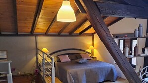 Un dormitorio acogedor con techo de madera, una cama con cabecera, lámparas de noche y una silla.