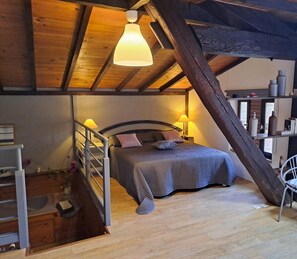 Un dormitorio acogedor con techo de madera, una cama con cabecera, lámparas de noche y una silla.