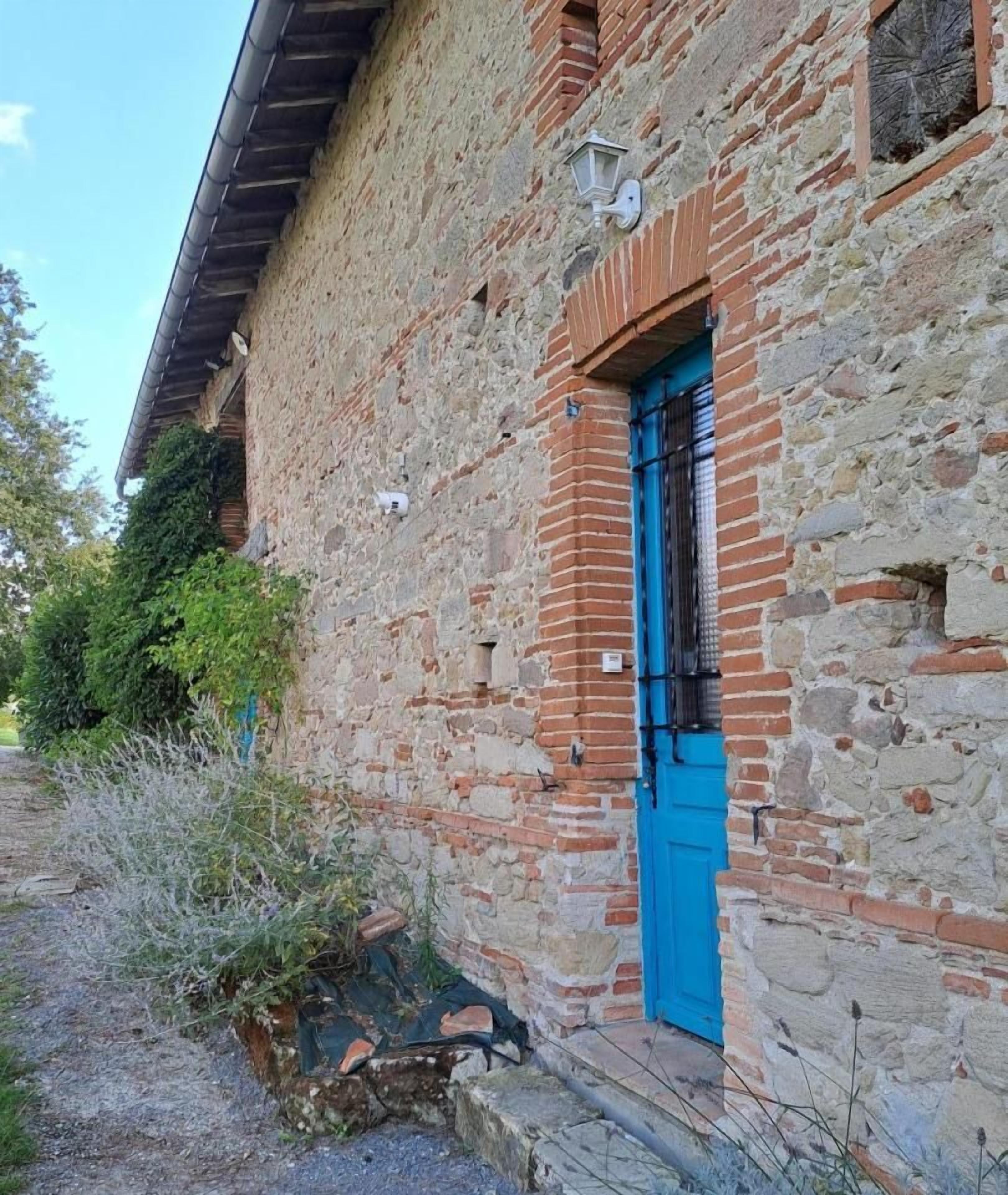 Un bâtiment rustique en pierre, avec une porte bleue et une petite fenêtre.