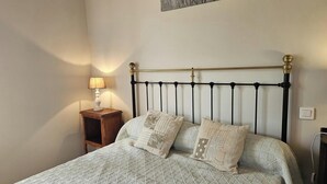 Een bed met een bedsprei met patroon, twee kussens, een nachtkastje met een lamp en een wandlamp.