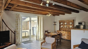 Een ruime woonkamer met houten plafond, een eettafel, stoelen, een televisie en een keuken met een magnetron.