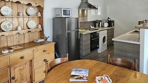 Een compacte keuken met een houten kastje, magnetron, koelkast, fornuis en wasmachine.