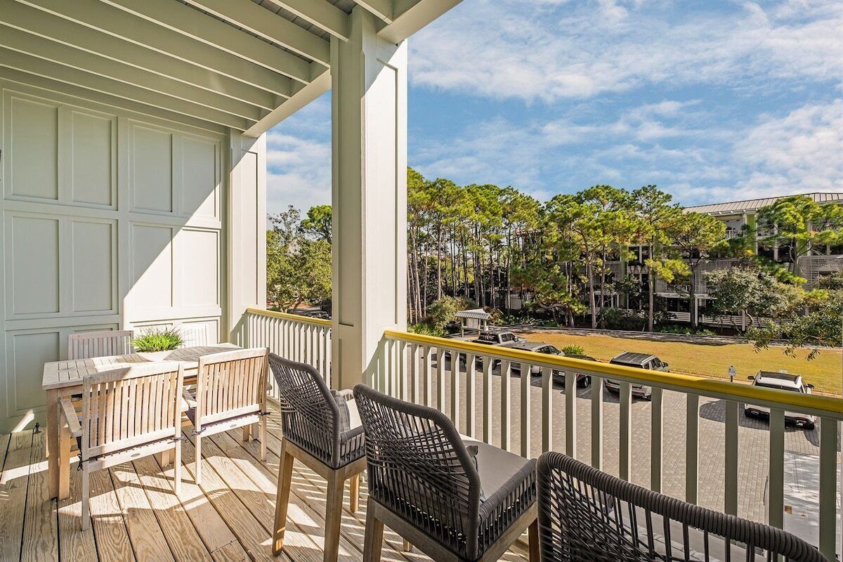 A balcony with a table and chairs, overlooking a parking area and buildings.