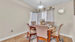 A dining area with a wooden table, four chairs, a vase with flowers, a chandelier, and a decorative mirror on the wall. - 3-bedroom house in charming North Las Vegas with AC (North Las Vegas)