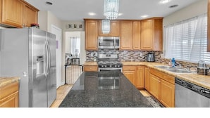 A kitchen with wooden cabinets, stainless steel appliances, a black granite countertop, and a chandelier. - 3-bedroom house in charming North Las Vegas with AC (North Las Vegas)