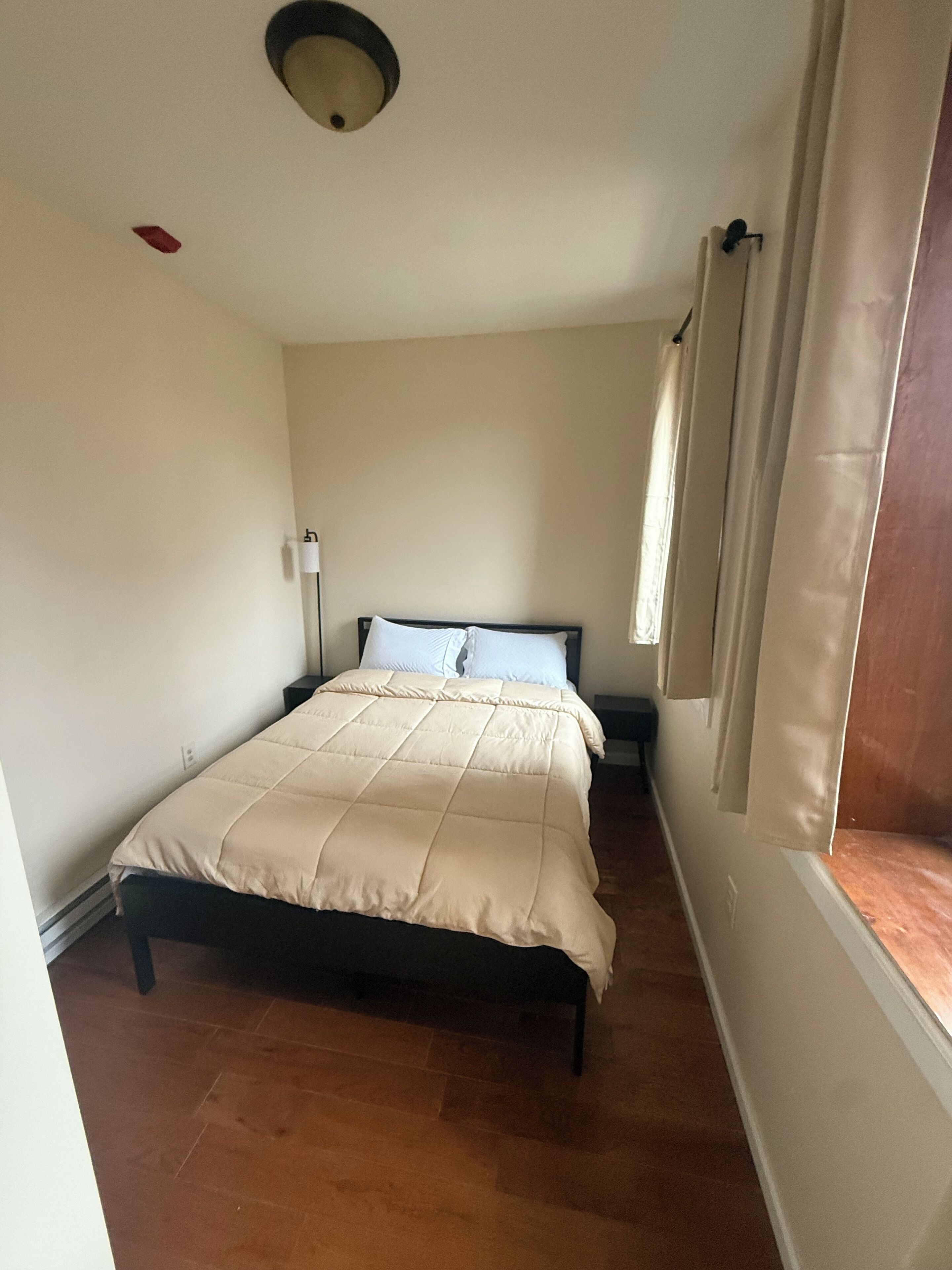 Een slaapkamer met een bed, een nachtkastje, een lamp en een raam met gordijnen.