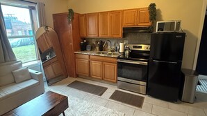 A modern kitchen with wooden cabinets, a black refrigerator, a microwave, and a stove. There is a window with a view of a building outside. - Pet friendly 1Bd In Arena District With Event Parking (Detroit)
