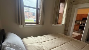A bedroom with a large bed, two windows, and a view of a brick building outside. - Pet friendly 1Bd In Arena District With Event Parking (Detroit)