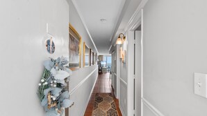A hallway with white walls, a patterned rug, and a decorative plant arrangement.