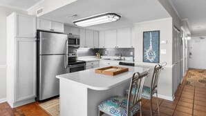 A modern kitchen with white cabinetry, stainless steel appliances, and a central island with bar stools.